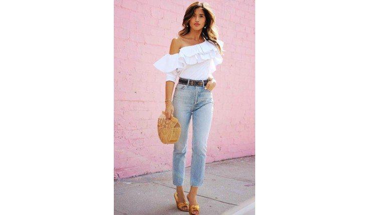 Mulher com jeans, blusa branca e bolsa de palha.