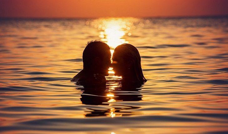 casal dentro do mar se beijando com o sol se pondo ao fundo
