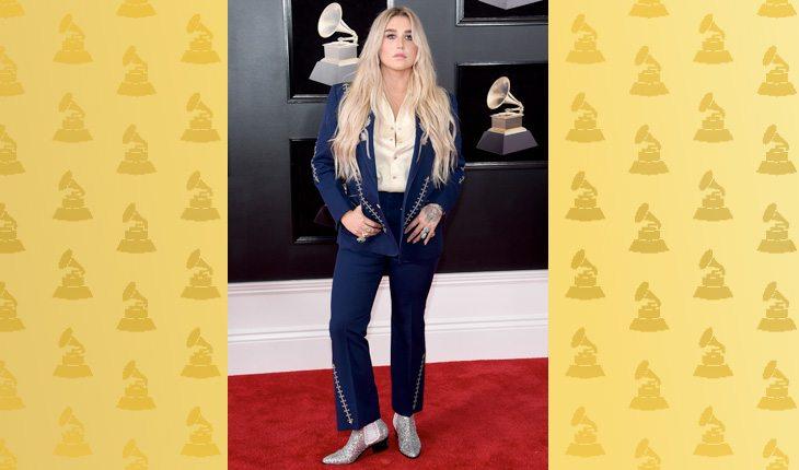 Grammy Awards 2018. Na foto, está a cantora Kesha com um terno azul marinho e uma bota brilhante