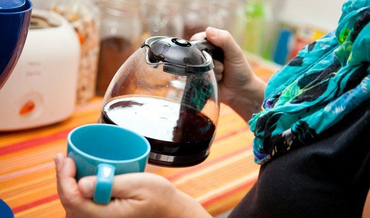 Mulher colocando café de cafeteira em xícara azul
