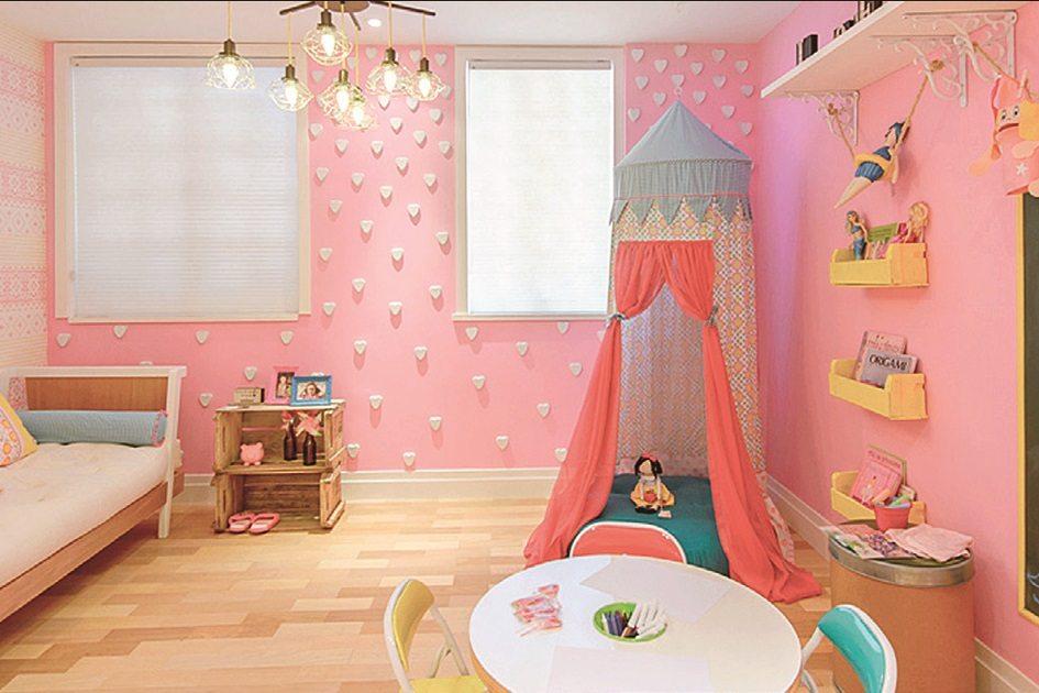 Quarto rosa com duas janelas ao fundo em uma parede com textura e la parede da direta há vários nichos e uma prateleira com brinquedos para proporcionar diversão para as crianças.