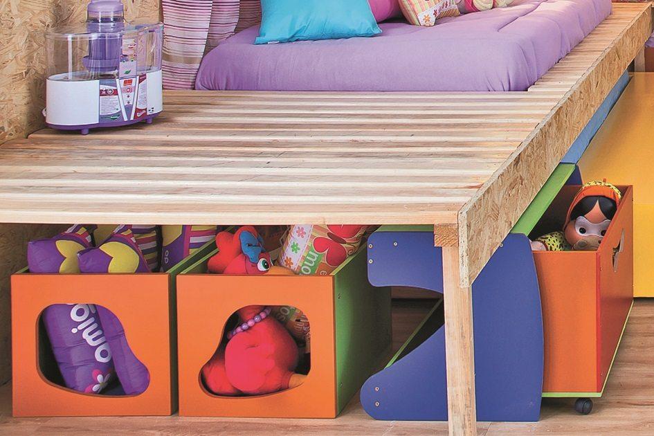Embaixo da cama feita de madeira, há várias caixas coloridas organizadoras com diversos ursos de pelúcia dentro para organizar o ambiente de diversão para as crianças.