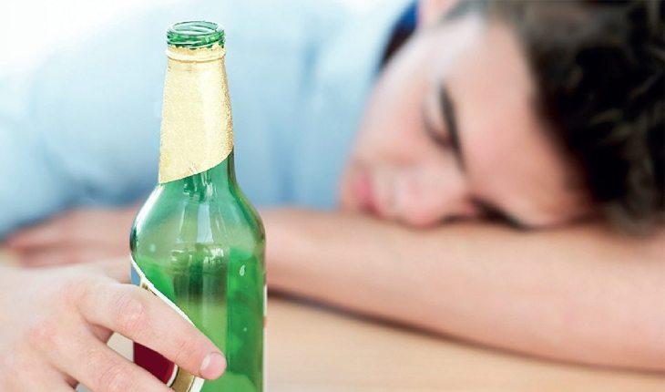 jovem dormindo em uma mesa segurando uma garrafa de cerveja