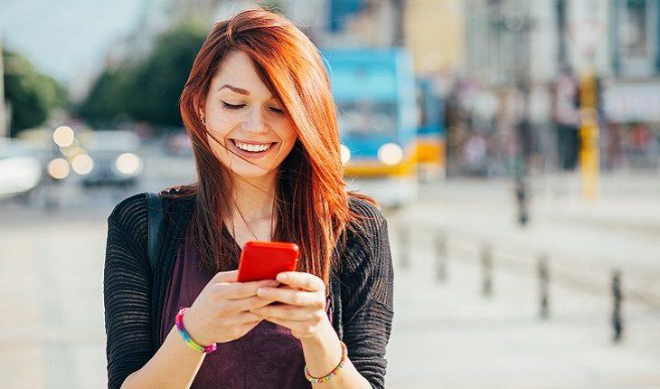 mulher sorrindo mexendo no celular no meio da rua