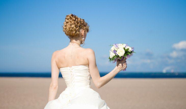 Noiva na praia segurando buquê de flores
