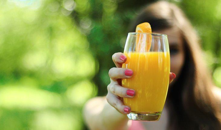 mulher segurando copo com suco de laranja