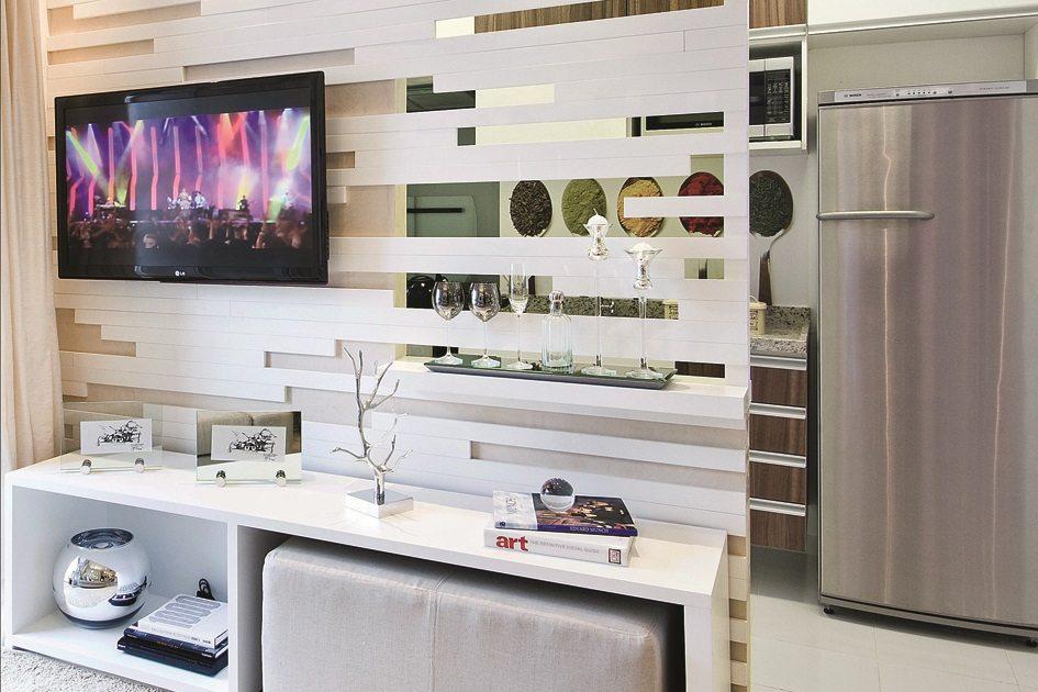 A decoração de ambientes integrados foi utilizada nesse cômodo através de um painel de tv branco vazado que dá para ver a cozinha.