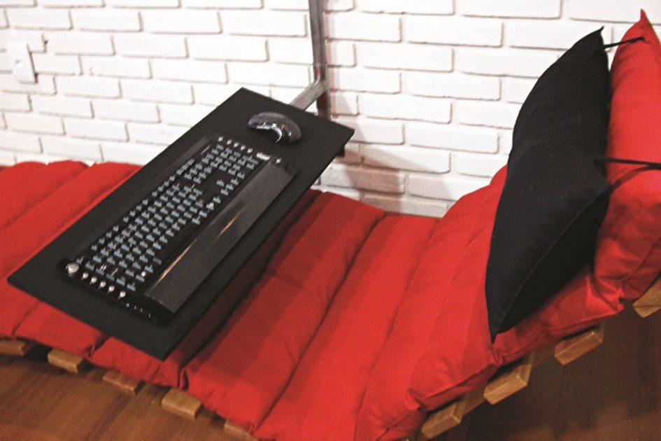 Cadeira com estofado vermelho e travesseiro preto, com um teclado de computador em uma mesinha sob a cadeira.