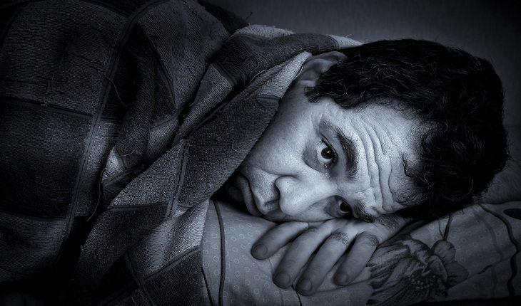 foto em preto e branco de um homem triste, deitado na cama