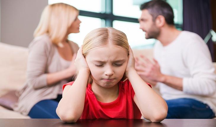 foto de uma menina tapando os ouvidos com os pais discutindo ao fundo