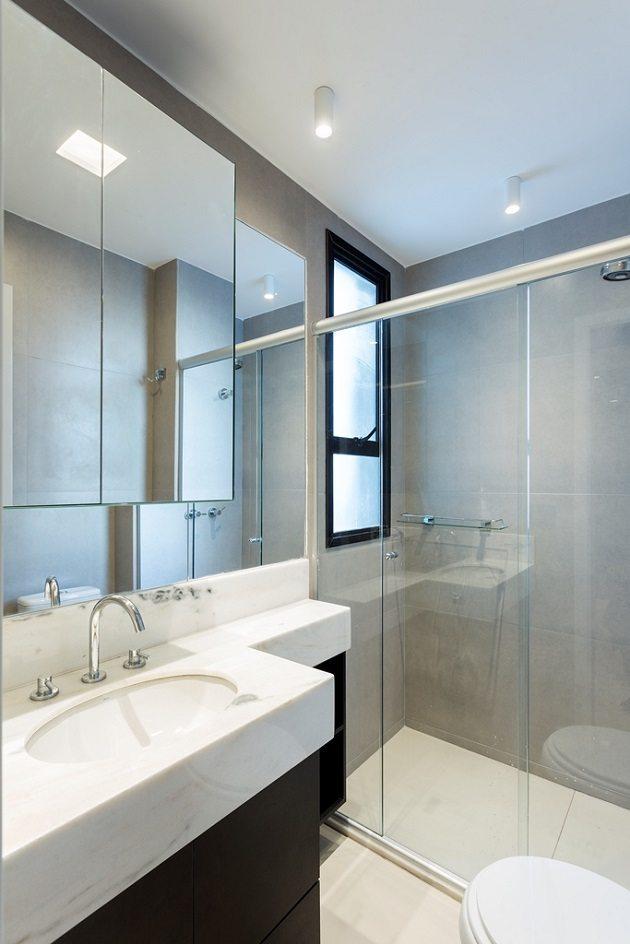 Banheiro claro em tons de cinza com armário abaixo da pia feito com marcenaria multiúso.