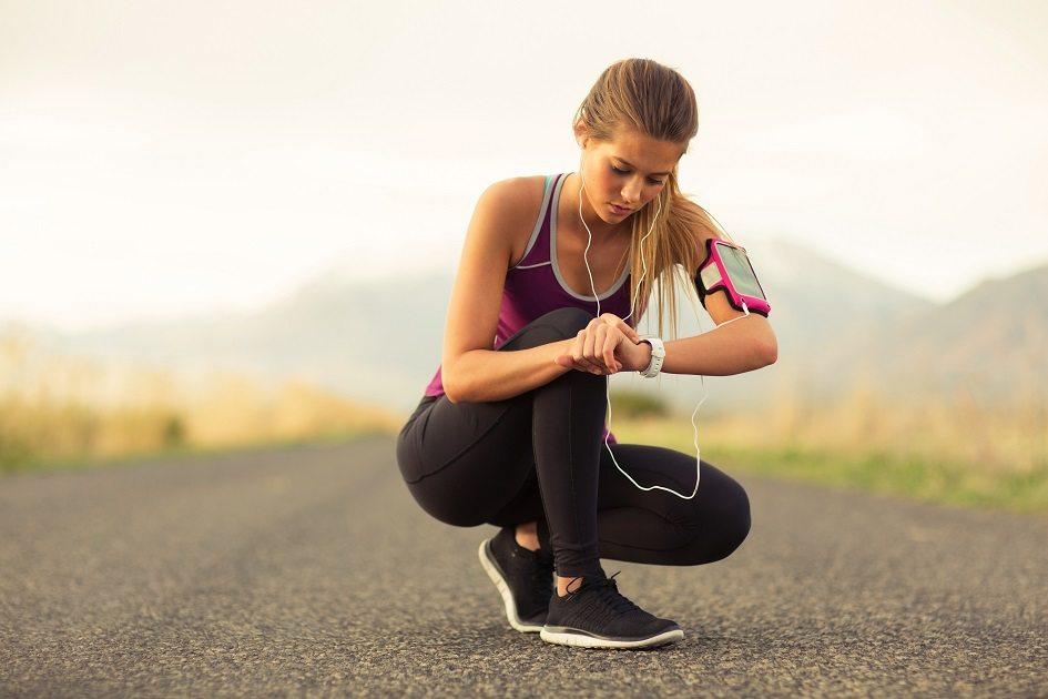 Mulher atleta agachada em uma rodovia olhando o relógio e vestida com roupa de ginástica após saber das propriedades da quinoa e seus benefícios pré e pós treino.