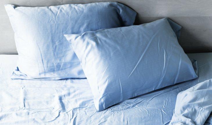 cama com lençol azul e dois travesseiros com fronhas azuis