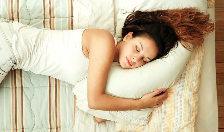 A foto mostra uma mulher dormindo em sua cama com um pijama branco