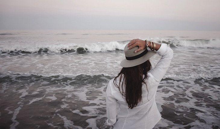 mulher a beira da praia segurando chapéu