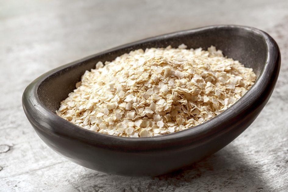 Recipiente de barro escuro em formato oval cheio de quinoa em flocos que não perdem as propriedades da quinoa em grãos.