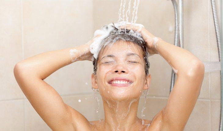 Mulher lavando o cabelo com espuma embaixo de um chuveiro