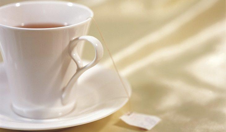 Xícara branco com chá de sachê em cima da mesa