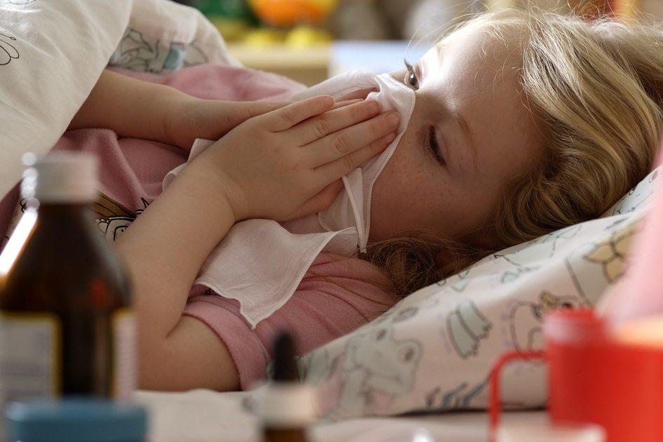 Criança menina e loira deitada na cama assoando o nariz.