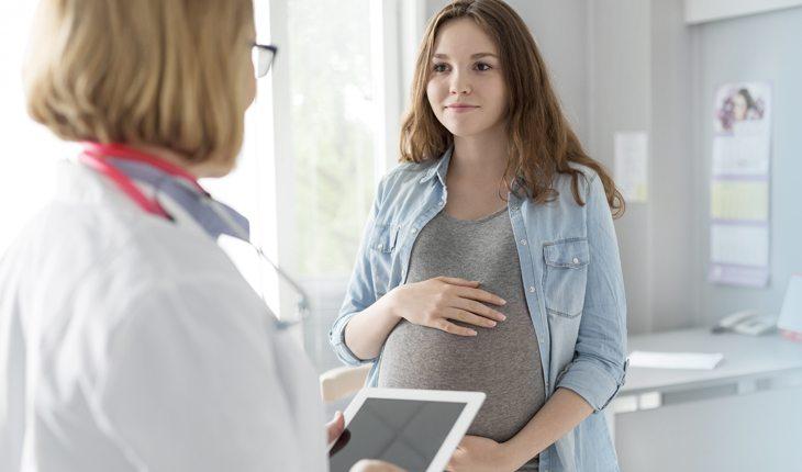 Na imagem, a adolescente está segurando a barriga grávida na médica. Idade para engravidar.