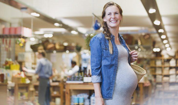 Na imagem, a mulher grávida sorri no mercado. Idade para engravidar.
