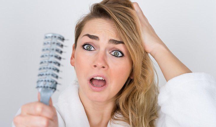 mulher escovando o cabelo e com a expressão assustada por estar vendo os fios na escova