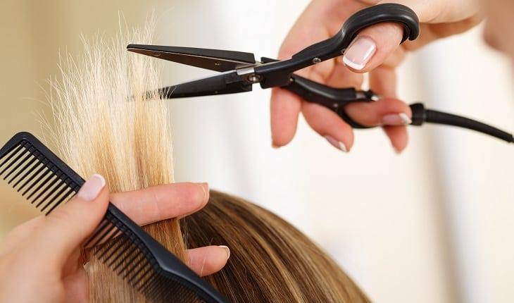 Mulher cortando as pontas de um cabelo loiro