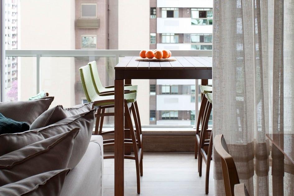 Varanda de um apartamento vista da sala, com mesa e cadeira de madeira