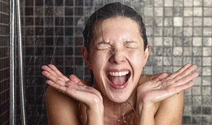Mulher embaixo do chuveiro com a boca aberta e olhos fechados semelhante a uma expressão de alegria