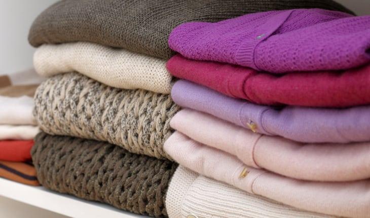Pilha de blusas de lã dobradas nas cores marrom, roxo, rosa e vermelho