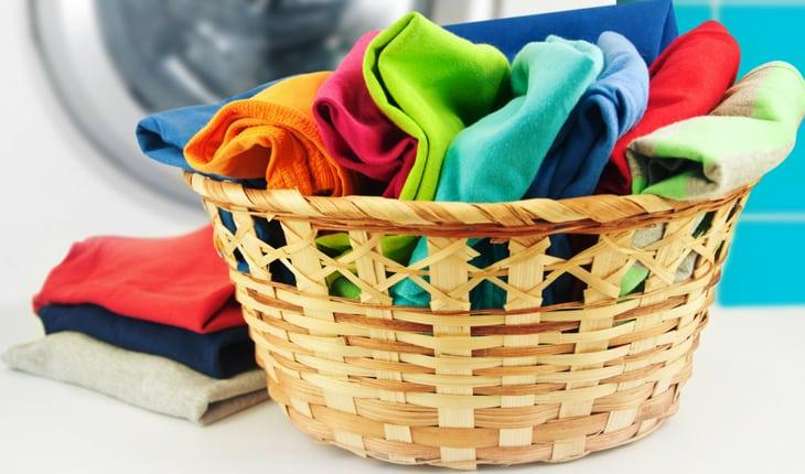 Cesto de palha com roupas coloridas sujas e máquina de lavar ao fundo
