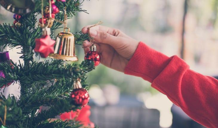 Mão pendurando bola de Natal em árvore