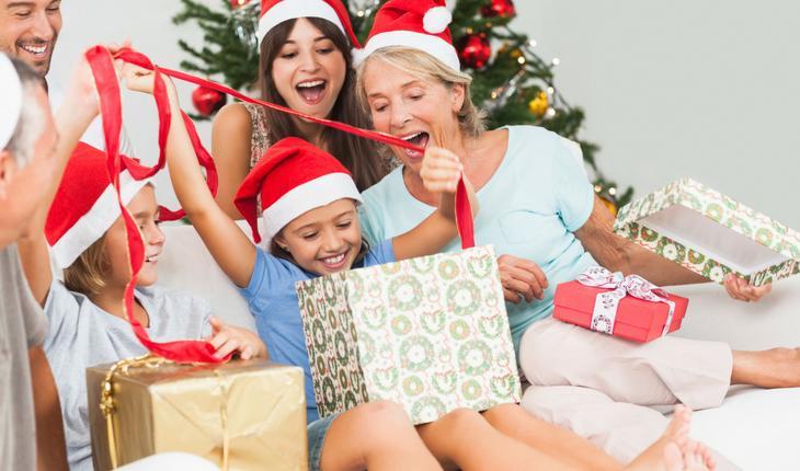 Família sentada em sofá com criança abrindo presente de Natal