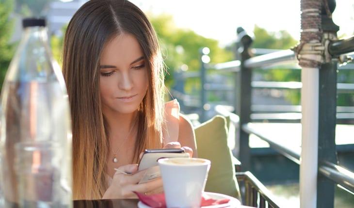 mulher mexendo no celular enquanto toma café