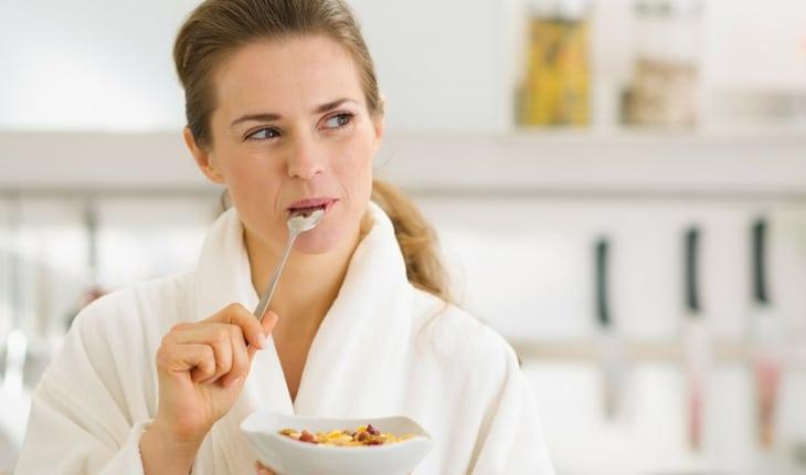 Mulher comendo cereal de café da manhã e vestindo roupão branco