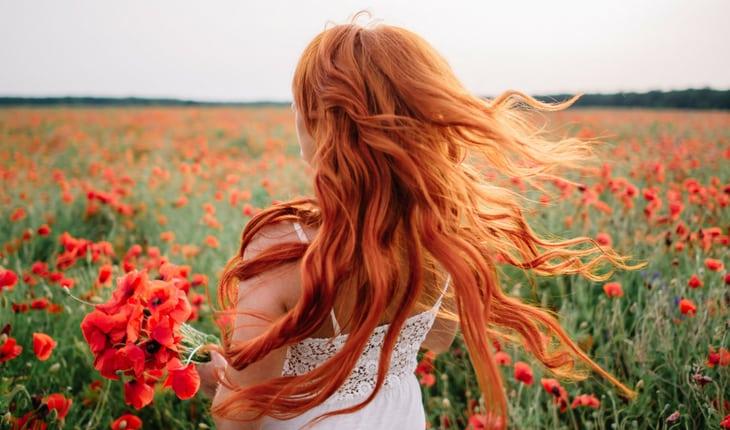 Mulher ruiva no campo com flores laranjas