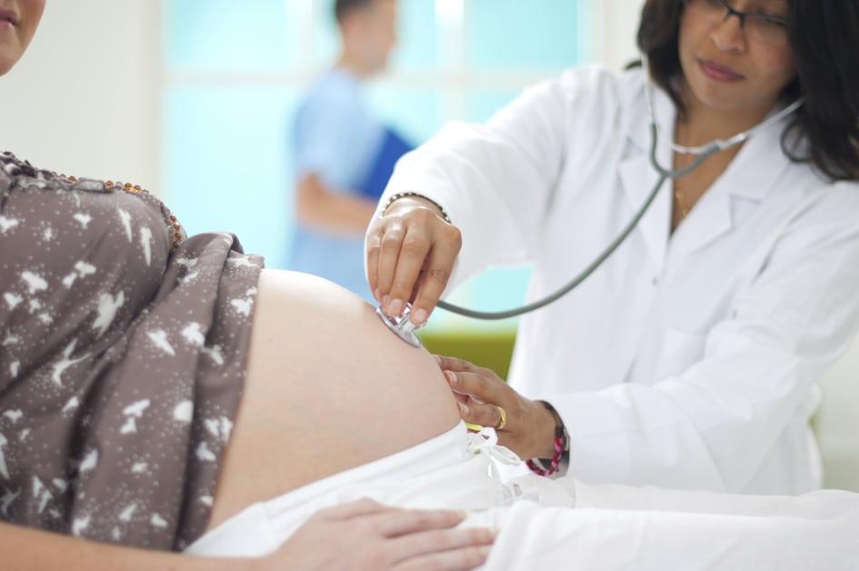Médica apoiando uma estetoscópio na barriga de uma mulher gravida para ilustrar o tema exames durante a gravidez