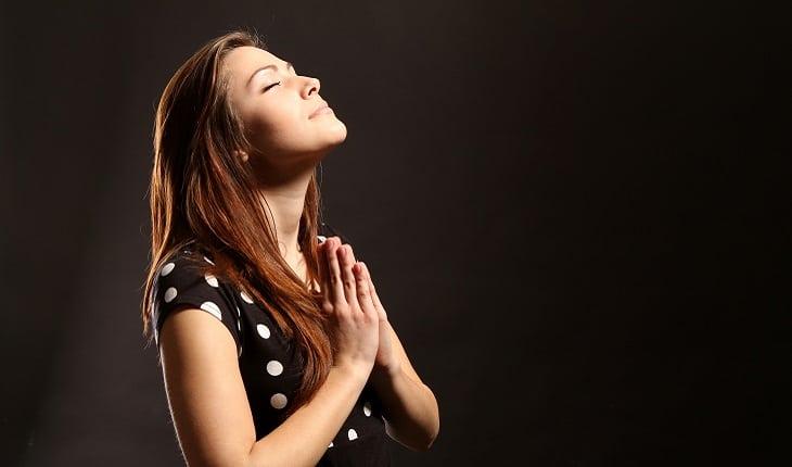 mulher rezando de olhos fechados com um fundo preto