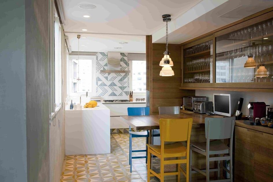 Cozinha com decoração amadeiradas, cadeiras coloridas, azulejos em tons alegres e armário de vidro