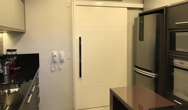 Foto de uma cozinha com armários escuros, mesa na cor berinjela e eletrodomésticos inox. Há uma porta de correr branca