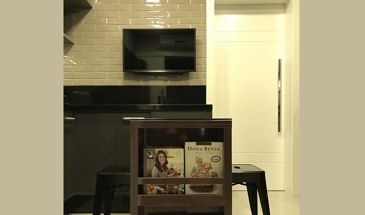 Foto de uma cozinha com armários escuros e mesa na cor berinjela. Há uma TV na parede lateral da mesa, uma porta de correr branca e brancos pretos