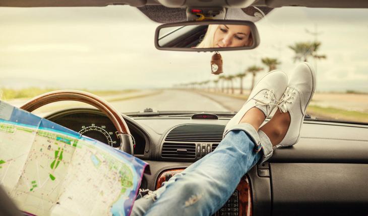 Mulher dentro de carro com pés no painel e olhando um mapa parada na estrada