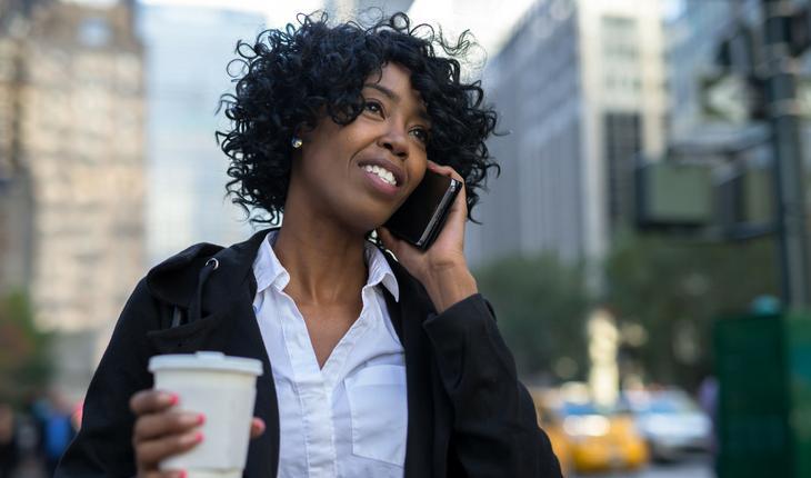 mulher negra empresária falando ao celular e segurando um copo de plástico no meio de uma rua