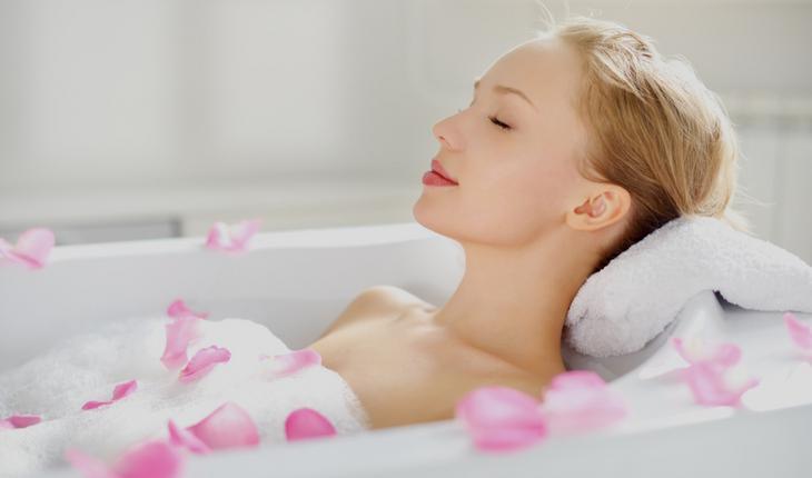 Mulher tomando banho na banheira com espuma e rosas