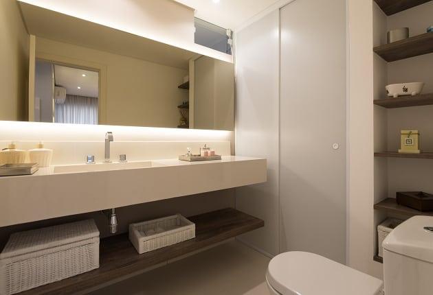 Foto do banheiro todo em tons beges com prateleiras que substituem armários em madeira