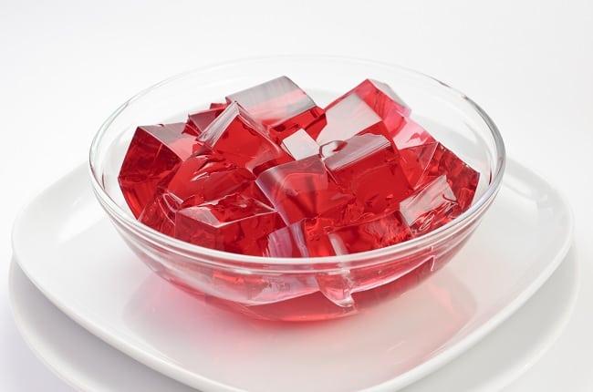 Cubos de gelatina vermelha em pote transparente sobre prato branco