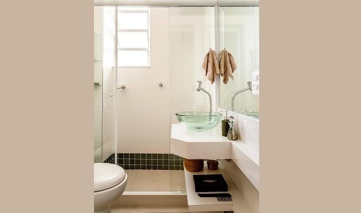 Fotos do banheiro com bancada branca e cuba de vidro, dentro do box a parede é revestida predominantemente de azulejo branco, com um filete na parte superior e inferior de azulejos menores na cor verde escuro