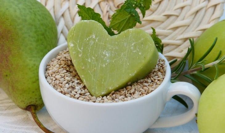 Sabonete verde em formato de coração, dentro de xícara branca com grãos cor bege.
