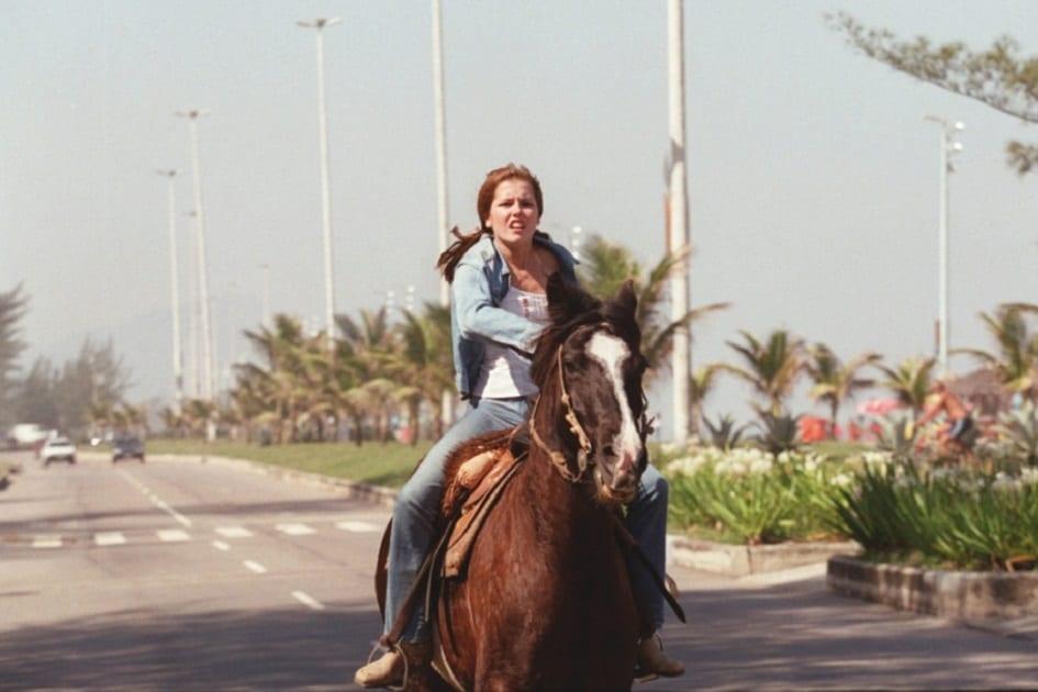 Personagens de Deborah Secco: Íris, de Laços de Família. Na cena, ela está montada em um cavalo, cavalgando pela rua.