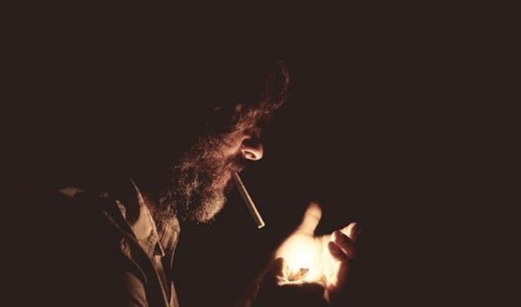 homem barbudo no escuro acendendo cigarro